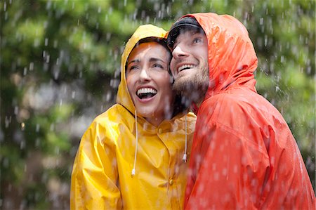 Happy couple in raincoats looking up at rain Stock Photo - Premium Royalty-Free, Code: 6113-06899635