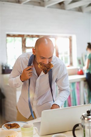 Businessman eating breakfast and using laptop Stock Photo - Premium Royalty-Free, Code: 6113-06908504