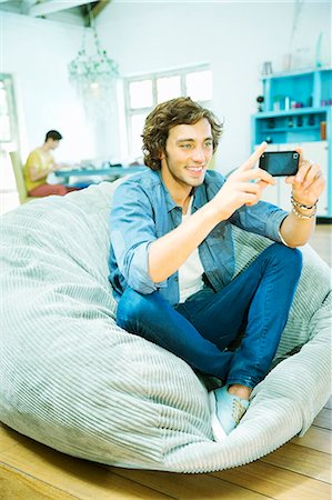 roommate (male) - Man using cell phone in beanbag chair Stock Photo - Premium Royalty-Free, Code: 6113-06908657