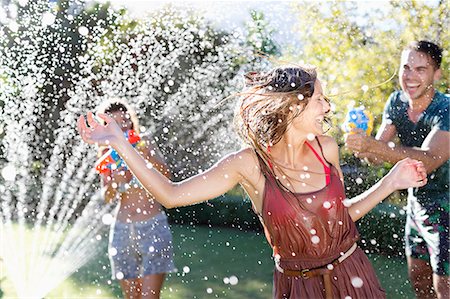 Friends playing with water guns in sprinkler Photographie de stock - Premium Libres de Droits, Code: 6113-06909340