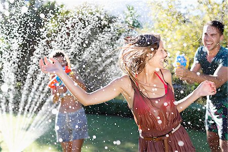 despreocupado - Friends playing with water guns in sprinkler Foto de stock - Sin royalties Premium, Código: 6113-06909340