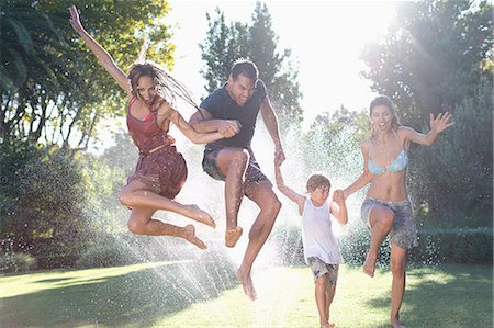 simsearch:614-08908362,k - Family jumping in sprinkler Photographie de stock - Premium Libres de Droits, Code: 6113-06909344