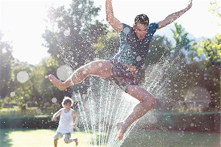 spraying - Father and son playing in sprinkler in backyard Stock Photo - Premium Royalty-Free, Code: 6113-06909353