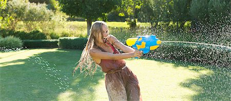 Girl playing with water gun in backyard Stock Photo - Premium Royalty-Free, Code: 6113-06909363
