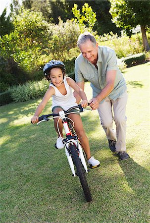 family in garden - Older man teaching granddaughter to ride bicycle Stock Photo - Premium Royalty-Free, Code: 6113-06909467