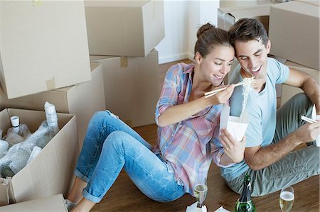 photo of a woman feeding her husband food - Couple sharing Chinese take out food in new house Foto de stock - Sin royalties Premium, Código: 6113-07147171