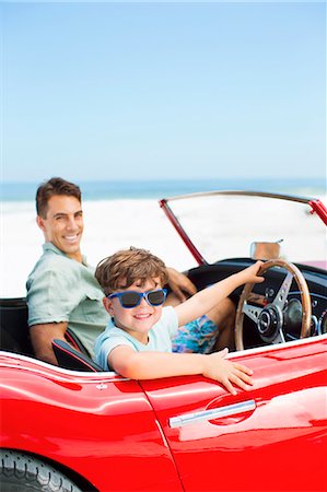 Boy sitting behind steering wheel of convertible with father at beach Stock Photo - Premium Royalty-Free, Code: 6113-07147771