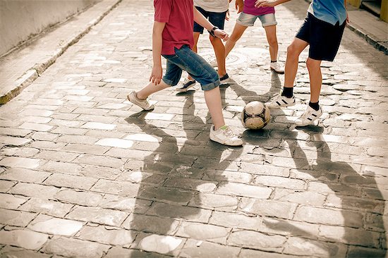 Children playing with soccer ball on cobblestone street Stock Photo - Premium Royalty-Free, Image code: 6113-07159149