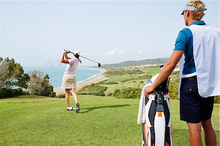 simsearch:6113-07159316,k - Caddy watching woman tee off on golf course overlooking ocean Stock Photo - Premium Royalty-Free, Code: 6113-07159207