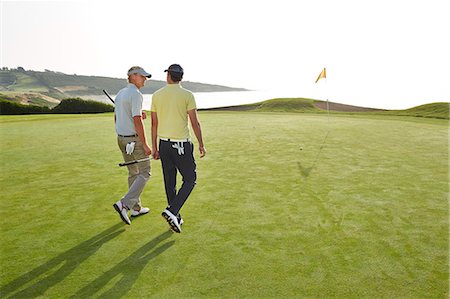 simsearch:6113-07159194,k - Men walking toward hole on golf course overlooking ocean Stock Photo - Premium Royalty-Free, Code: 6113-07159340