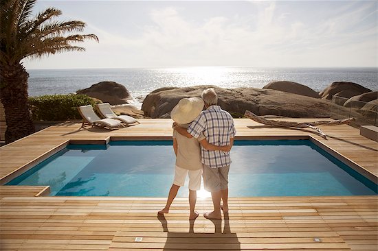 Senior couple hugging by modern pool overlooking ocean Stock Photo - Premium Royalty-Free, Image code: 6113-07159487