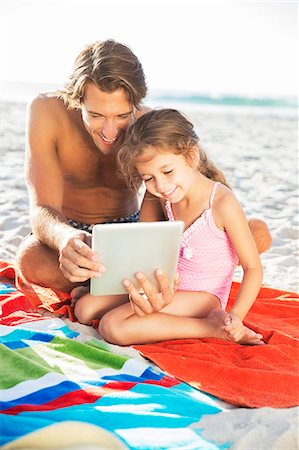 family on beach swimsuits - Father and daughter using digital tablet on beach Stock Photo - Premium Royalty-Free, Code: 6113-07159599