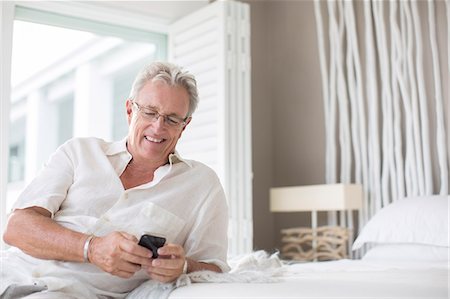 eyes lowered - Older man using cell phone on bed Stock Photo - Premium Royalty-Free, Code: 6113-07159695