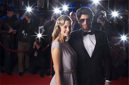 Serious celebrity couple on red carpet with paparazzi in background Photographie de stock - Premium Libres de Droits, Code: 6113-07159911