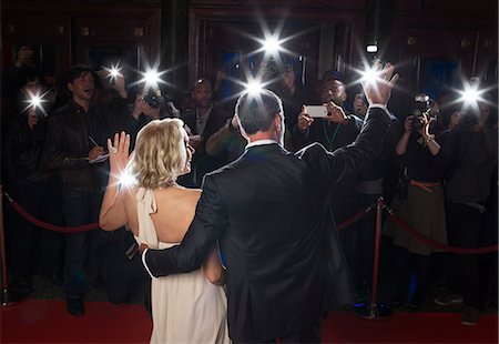 paparazzi camera flash at night - Rear view of well dressed couple waving to paparazzi at red carpet event Stock Photo - Premium Royalty-Free, Code: 6113-07160003