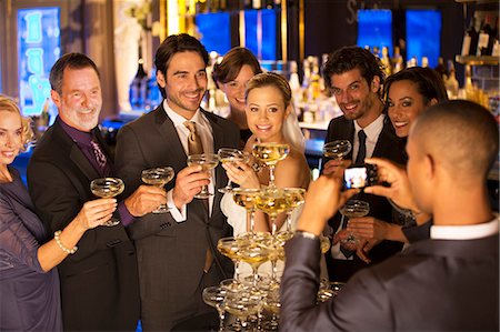 Man photographing bride and groom with friends at champagne pyramid Foto de stock - Sin royalties Premium, Código: 6113-07160036