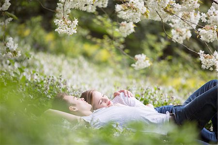 simsearch:6116-08916123,k - Couple laying in grass under tree with white blossoms Photographie de stock - Premium Libres de Droits, Code: 6113-07160615