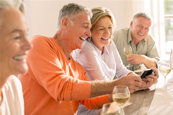 Senior couples drinking wine and looking at cell phone Stock Photo - Premium Royalty-Free, Image code: 6113-07242055