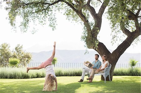 reading nature - Couple watching daughter do cartwheel outdoors Stock Photo - Premium Royalty-Free, Code: 6113-07242014
