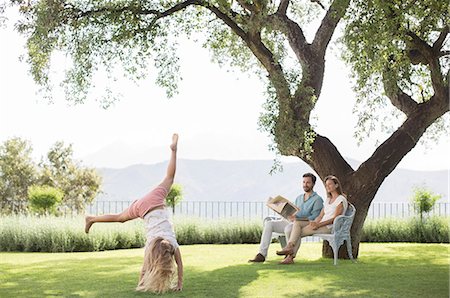 summer family backyard - Couple watching daughter do cartwheel outdoors Stock Photo - Premium Royalty-Free, Code: 6113-07242014