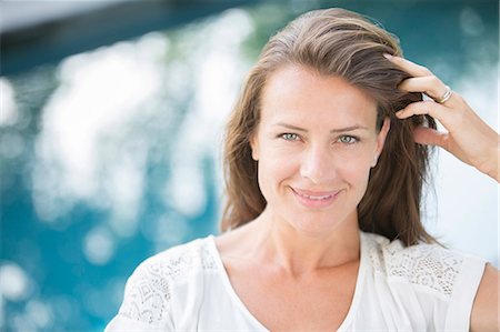 single 30 - Woman smiling with hand in hair at poolside Stock Photo - Premium Royalty-Free, Code: 6113-07242120