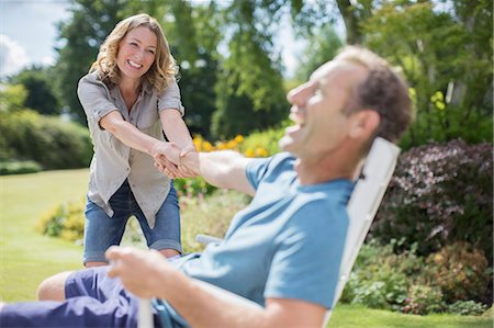 Woman pulling boyfriend out of chair in backyard Stock Photo - Premium Royalty-Free, Code: 6113-07242377