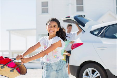 family loading car - Happy girl swinging beach bag outside car in sunny driveway Stock Photo - Premium Royalty-Free, Code: 6113-07242582