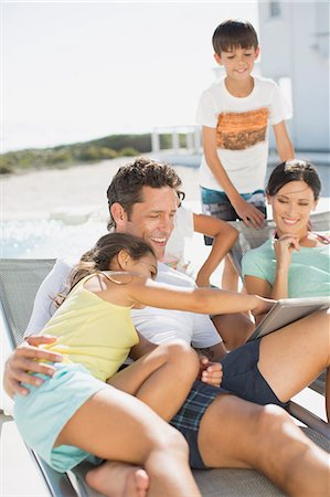 Family using digital tablet on lounge chairs at poolside Stock Photo - Premium Royalty-Free, Code: 6113-07242511