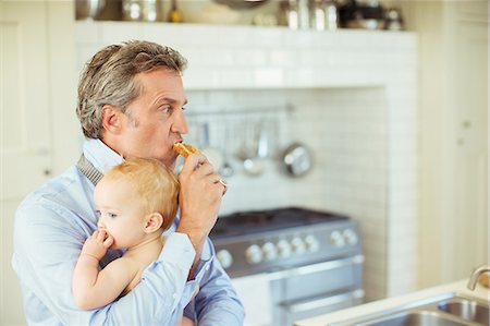 papa multitasking - Father holding baby and eating breakfast Stock Photo - Premium Royalty-Free, Code: 6113-07242896