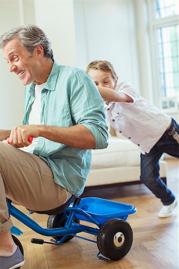 Boy pushing father on tricycle indoors Stock Photo - Premium Royalty-Free, Image code: 6113-07242962