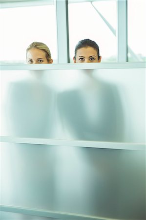 Businesswomen peeking over half wall in office Foto de stock - Sin royalties Premium, Código: 6113-07243085