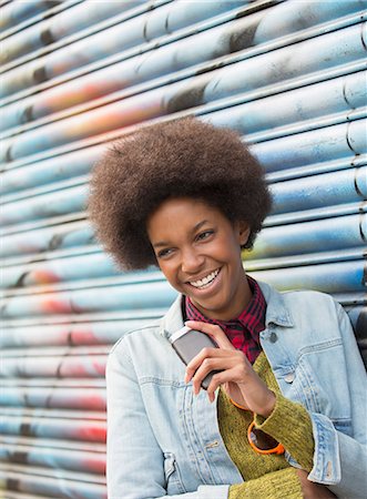 people laughing smart phones outdoor - Woman with cell phone smiling against graffiti wall Foto de stock - Sin royalties Premium, Código: 6113-07542475