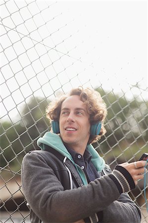 Man listening to headphones against chain link fence Stock Photo - Premium Royalty-Free, Code: 6113-07542530
