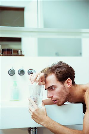 Hungover man watching effervescent tablets in bathroom Photographie de stock - Premium Libres de Droits, Code: 6113-07543009