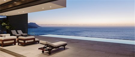 Modern patio and infinity pool overlooking ocean at sunset Foto de stock - Sin royalties Premium, Código: 6113-07543352