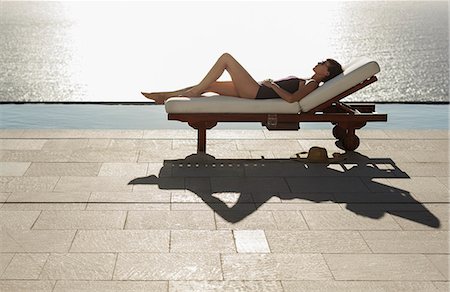 simsearch:6113-06898828,k - Woman sunbathing in lounge chair at poolside overlooking ocean Foto de stock - Sin royalties Premium, Código: 6113-07543386