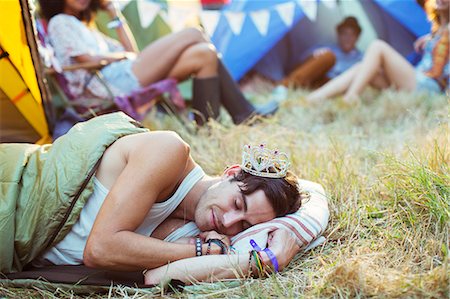 Man in tiara sleeping in sleeping bag outside tents at music festival Stock Photo - Premium Royalty-Free, Code: 6113-07564877