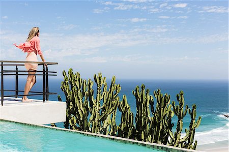 simsearch:6113-07565219,k - Woman standing on poolside balcony overlooking ocean Stock Photo - Premium Royalty-Free, Code: 6113-07565212