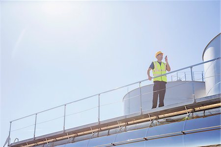 simsearch:6113-07565427,k - Worker using walkie-talkie on platform next to silage storage towers Stock Photo - Premium Royalty-Free, Code: 6113-07565366