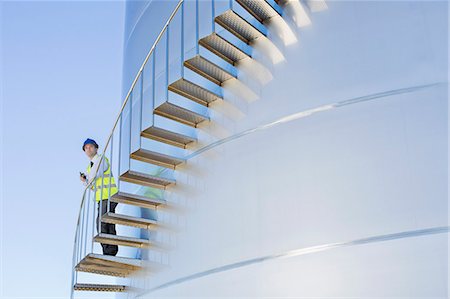 Worker with walkie-talkie standing on stairs winding along silage storage tower Foto de stock - Royalty Free Premium, Número: 6113-07565388