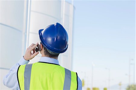 Worker talking on cell phone and looking up at silage storage towers Stock Photo - Premium Royalty-Free, Code: 6113-07565336