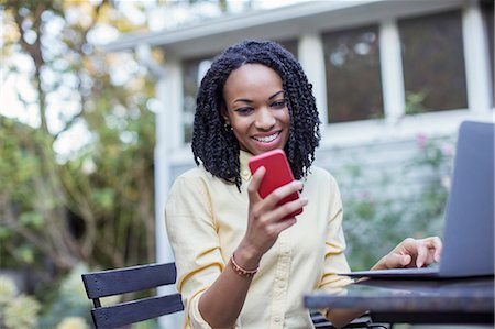 simsearch:6113-07790572,k - Smiling woman using cell phone and laptop on patio Foto de stock - Sin royalties Premium, Código: 6113-07565584