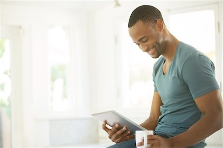 reading ebook - Smiling man drinking coffee and using digital tablet Stock Photo - Premium Royalty-Free, Code: 6113-07565589