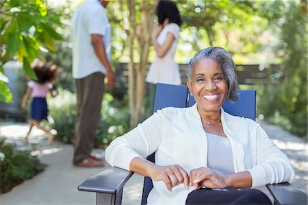 quattro generazioni - Portrait of smiling senior woman on patio with family in background Fotografie stock - Premium Royalty-Free, Codice: 6113-07565538