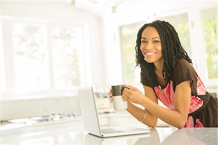 simsearch:6113-08321133,k - Portrait of smiling woman drinking coffee at laptop in kitchen Stock Photo - Premium Royalty-Free, Code: 6113-07565606