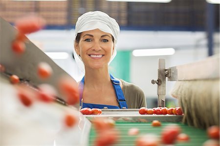 Portrait of smiling worker examining tomatoes at conveyor belt in food processing plant Stock Photo - Premium Royalty-Free, Code: 6113-07589256