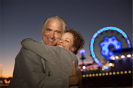 Portrait of couple hugging outside amusement park at night Stock Photo - Premium Royalty-Free, Code: 6113-07589378