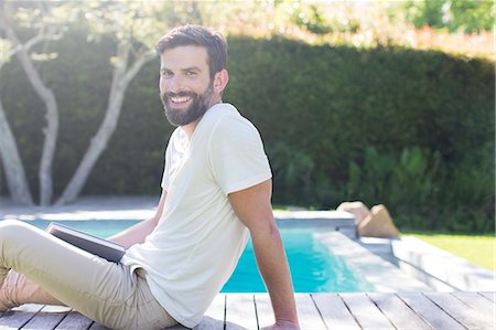 Smiling man relaxing on wooden deck by swimming pool Foto de stock - Sin royalties Premium, Código: 6113-07790560