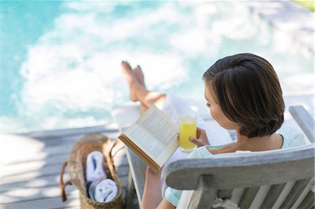 High angle view of woman reading and drinking juice by swimming pool Stock Photo - Premium Royalty-Free, Code: 6113-07790516