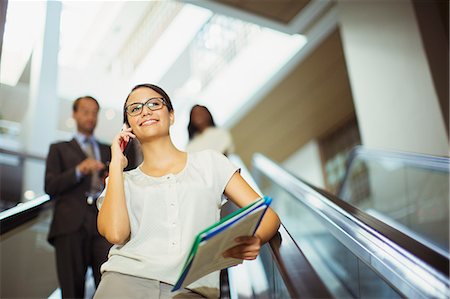 simsearch:6113-07791454,k - Businesswoman talking on cell phone while going down escalator Photographie de stock - Premium Libres de Droits, Code: 6113-07791416